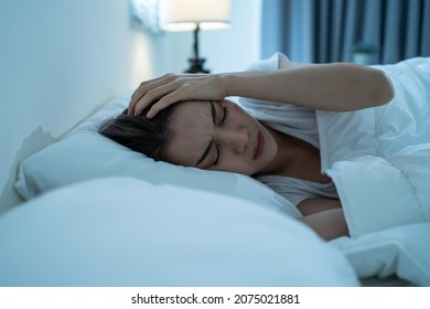 Asian Beautiful Upset Depressed Sick Girl Lying Down On Bed In Bedroom. Attractive Unhappy Young Woman In Pajamas Feel Sad Lonely And Upset With Headache And Cannot Sleep In Dark Night Room At Home.