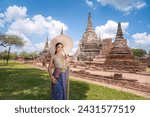 Asian beautiful wearing Thai traditional dress holding umbrella in ancient temple with old pagoda background.