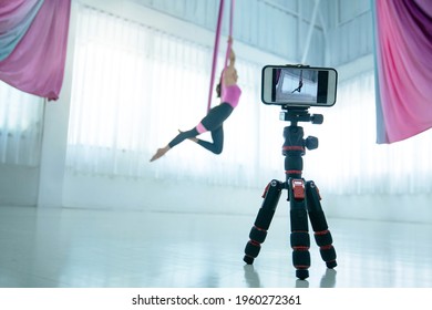 Asian beautiful woman doing aerial dance practice in hammock at studio, and uses digital smartphone camera make online live stream, selective focus - Powered by Shutterstock