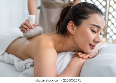 Asian Beautiful Woman Enjoy Thai Hot Compress Massage With Herbal Bags. Attractive Girl Lying On Massage Table, Feel Happy And Relax During Back Physiotherapy From Masseuse For Body Care In Spa Salon.