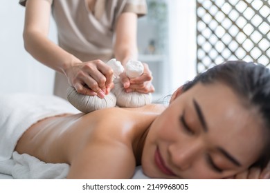 Asian beautiful woman enjoy thai hot compress massage with herbal bags. Attractive girl lying on massage table, feel happy and relax during back physiotherapy from masseuse for body care in spa salon.