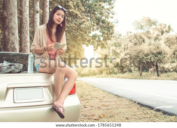 An asian\
beautiful woman get lost and sitting on her broken car beside the\
street while traveling alone in summer\
time.
