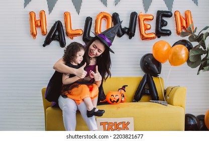 Asian Beautiful Woman Or Mother And Little Caucasian Sweet Girl Wearing And Dressing Up Halloween Costume With Hats, Playing Together With Fun, Smiling With Happiness, Celebrating Party At Home