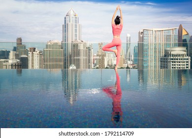 Asian beautiful woman in pink sports uniform doing a yoga exercise on hotel rooftop with Bangkok city view and skyscraper background. - Powered by Shutterstock