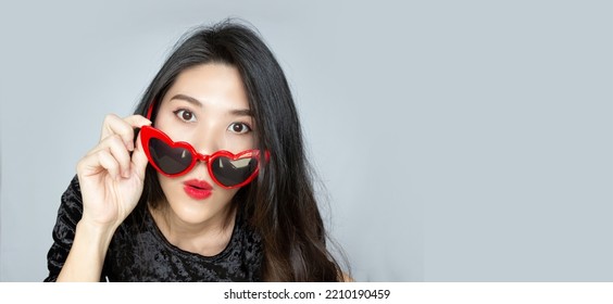 Asian Beautiful Woman Is Puckering Lip And Wearing Red Eyes Glasses With Amazed, Surprised, Unbelievable Face While  See Promotion Sale Or News