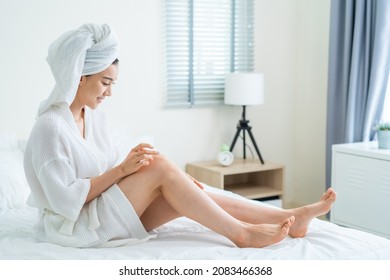 Asian Beautiful Woman Put Smooth And Soft Skin Care On Legs In Bedroom. Attractive Girl Touches Her Knee And Applying Cream Lotion For Rejuvenation With Gentle. Beauty, Skin Care And Health Concept.