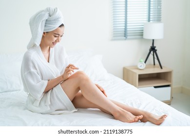 Asian Beautiful Woman Put Smooth And Soft Skin Care On Legs In Bedroom. Attractive Girl Touches Her Knee And Applying Cream Lotion For Rejuvenation With Gentle. Beauty, Skin Care And Health Concept.