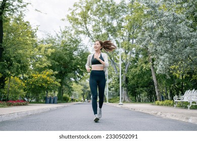 Asian beautiful woman running in a park for health, wellness and outdoor exercise. Nature, sports and female athlete runner doing cardio workout in garden. Healthy Concept.