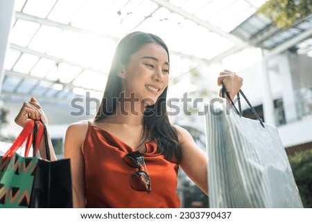 Asian beautiful woman shopping goods outdoor alone in department store. Attractive young girl holding shopping bags while walking with happiness enjoying purchasing goods in shopping mall center.