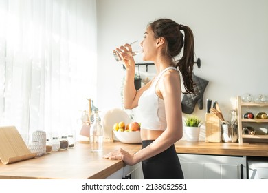 Asian beautiful woman in sportswear drink water after exercise at home. Young thirsty active sport girl takes a sips of clean mineral natural in cup after workout for health care in kitchen in house. - Shutterstock ID 2138052551