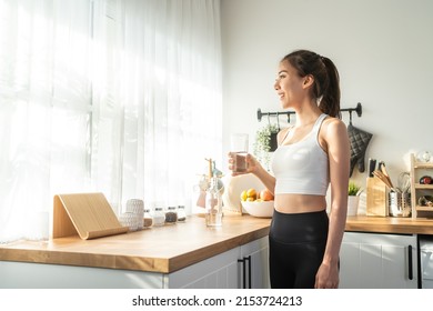 Asian beautiful woman in sportswear drink water after exercise at home. Young thirsty active sport girl takes a sips of clean mineral natural in cup after workout for health care in kitchen in house. - Shutterstock ID 2153724213