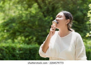 Asian Beautiful Woman Wearing A White Dress, Happy, Relaxed With Eating Delicious Ice Cream In The Park. In The Summer, The Happy Smile Of The Model Laughs, Not Looking At The Camera.