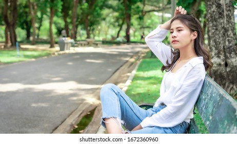 Asian beautiful woman with yellow skin, long black hair, wearing a white shirt, jeans,Sitting on a green bench showing emotions in the morning nature park