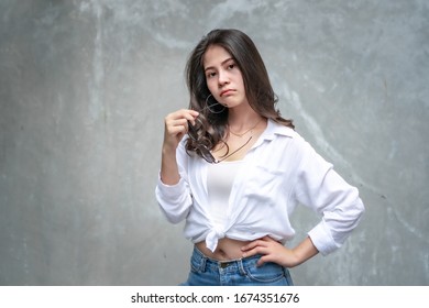 Asian beautiful woman with yellow skin, long black hair, wearing a white shirt, jeans showing her emotions.  Cement wall background