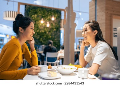 Asian beautiful women having dinner with friend in restaurant together. Attractive young girl feeling happy and relax, having fun talking and eating food at their table in dining room in cafeteria. - Powered by Shutterstock