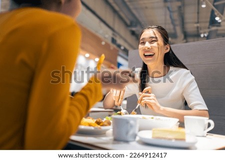 Asian beautiful women having dinner with friend in restaurant together. Attractive young girl feeling happy and relax, having fun talking and eating food at their table in dining room in cafeteria.