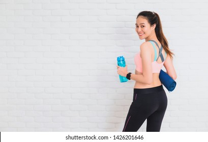 Asian Beautiful Women Holding Water Bottle And Yoga Mat After Play Yoga And Exercise On White Brick Wall Background With Copy Space.Exercise For Lose Weight,increase Flexibility And Tighten The Shape.