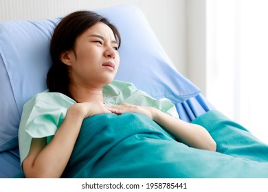 Asian Beautiful Young Female Patient Lying On Bed In Hospital And Touching Her Chest With Pain While Being Heart Disease. Medical Treatment And Health Concept