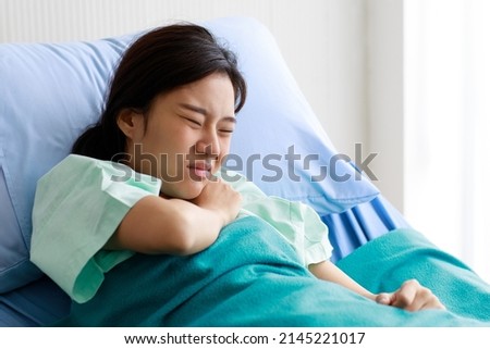 Asian beautiful young female patient lying on bed in hospital and touching her chest with pain while being heart disease. Medical Treatment and Health Concept