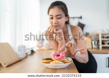 Asian beautiful young girl hungry and want to eat donut in kitchen. Attractive woman wear sport cloth feeling famished after exercies and pick up junk food unhealthy to eat, Food and health concept.