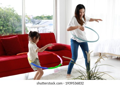 Asian beautiful young long black hair single mom stand smile playing hula hoop together with little cute daughter girl next to red sofa and bed in living bedroom with clear glass windows background. - Powered by Shutterstock