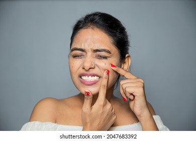 Asian beautiful young woman having skin problems squeezing pimples on her face, studio shot on gray
background, with copy space.