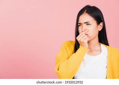 Asian beautiful young woman unhappy what a smell disgust expression squeezing nose with fingers. Female have something stinks bad smell situation, studio shot isolated on pink background, Healthcare