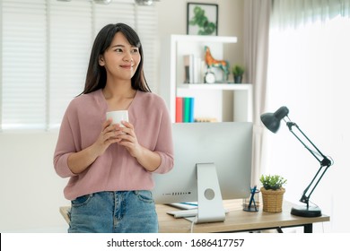 Asian beautiful young woman work from home working on computer and drinking coffeewhile relax from her work standing in living room at home. Social distancing lifestyle in house.
 - Powered by Shutterstock