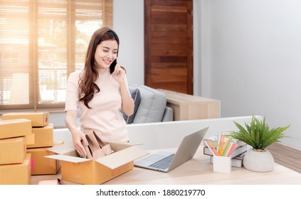 Asian beauty Checking the laptop order via the internet. And pack the paper box With a happy smiling face, being a new normal online business - Shutterstock ID 1880219770