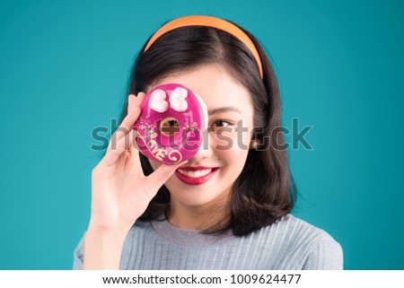 Asian beauty girl holding pink donut against her eye. Retro joyful woman with sweets, dessert standing over blue background.