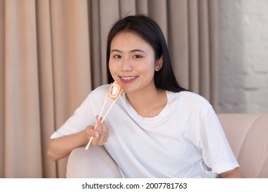 Asian Beauty Model Girl Eating Sushi Roll, Healthy Japanese Food. Beautiful Woman Holding Chopsticks With Philadelfia Roll At Apartment Home Living Room Interior