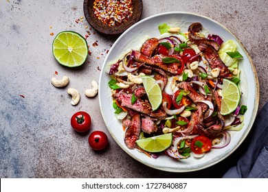 Asian beef salad with vegetables and nuts in a white bowl on a dark background. Asian food concept.