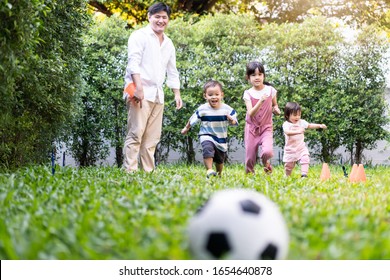 Asian big family playing in garden playground at home together. Children running to kick and catch football on green grass with father feels fun. Happy family and sibling enjoy love activity concept.
