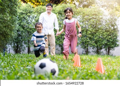 Asian Big Family Playing In Garden Playground At Home Together. Children Running To Kick And Catch Football On Green Grass With Father Feels Fun. Happy Family And Sibling Enjoy Love Activity Concept.