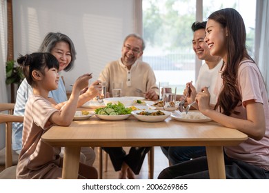 Asian Big Happy Family Spend Time Have Lunch On Dinner Table Together. Little Kid Daughter Enjoy Eating Foods With Father, Mother And Grandparents. Multi-Generation Relationship And Activity In House