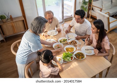 Asian Big Happy Family Spend Time Have Lunch On Dinner Table Together. Little Kid Daughter Enjoy Eating Foods With Father, Mother And Grandparents. Multi-Generation Relationship And Activity In House