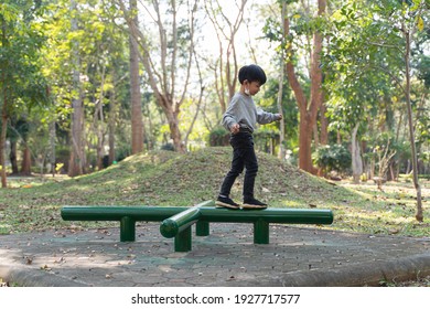 Asian Boy About 5 Years Old With Face Mask Under His Chin Playing And Having Fun With Balance Exercise At Kid Training Playground