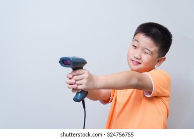 Asian Boy Aim A Fake Gun Made With Barcode Scanner, Studio Shot, On Gray Wall Background With Soft Shadow