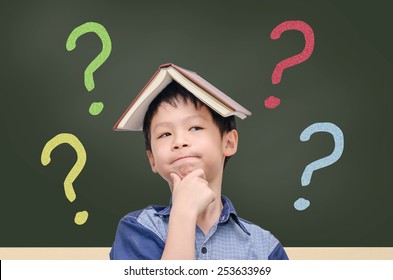 Asian Boy With Book On Head Thinking In Front Of Chalkboard With Question Mark