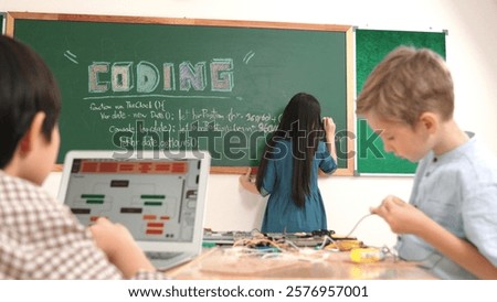 Asian boy coding program while caucasian friend fixing electric board at STEM class. Energetic student standing blackboard while writing coding engineering prompt and programing AI software. Pedagogy.
