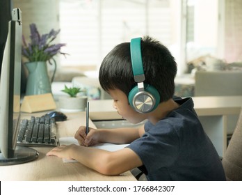 Asian Boy Concentrates On E-learning During Covid-19 Pandemic And Social Distancing Measures, Online Remote Learning With Computer Base Studying,    Doing Homework With Computer At Home.