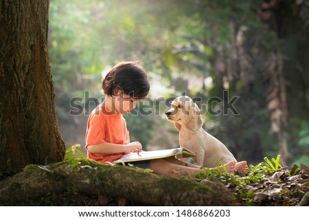 Asian boy and dog. Kid read book. Child and puppy under tree. American Cocker Spaniel home pet. Domestic animal. School and education. Nature and park. Early learning. Summer outdoor. Best friends. 