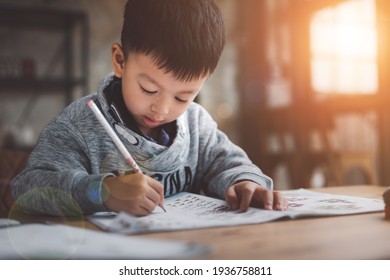 Asian Boy Doing homework with the intention. Child boy holding pencil writing, A boy drawing on white paper at the table, Elementary school and home schooling, Distance Education concept. - Powered by Shutterstock