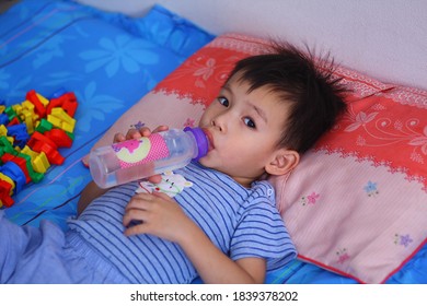 Asian Boy Drinking Water From Bottle Lying On Bed.