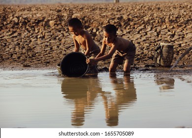 An Asian boy in a dry area is using a plastic bucket to draw water from the final water source. Concept of shortage of clean water from global warming