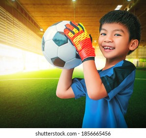 Asiatischer Junge ist ein Fußballsportler, der Handschuhe trägt und einen Fußball-Ball für das Jugendsportkonzept hält.