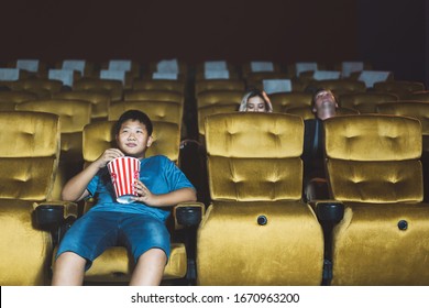 Asian boy go to the cinema. Alone in theater sad face and eating popcorn no parent. Background with couple people. - Powered by Shutterstock