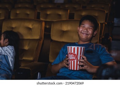 Asian Boy Holding Popcorn Watching A Movie In The Cinema.