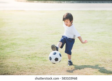 Asian Boy Kicking Football On The Field