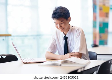 Asian boy with laptop in school. Student in classroom. Teenager in uniform doing homework with computer in library. Teen child studying for class. Kids study. Back to school. - Powered by Shutterstock